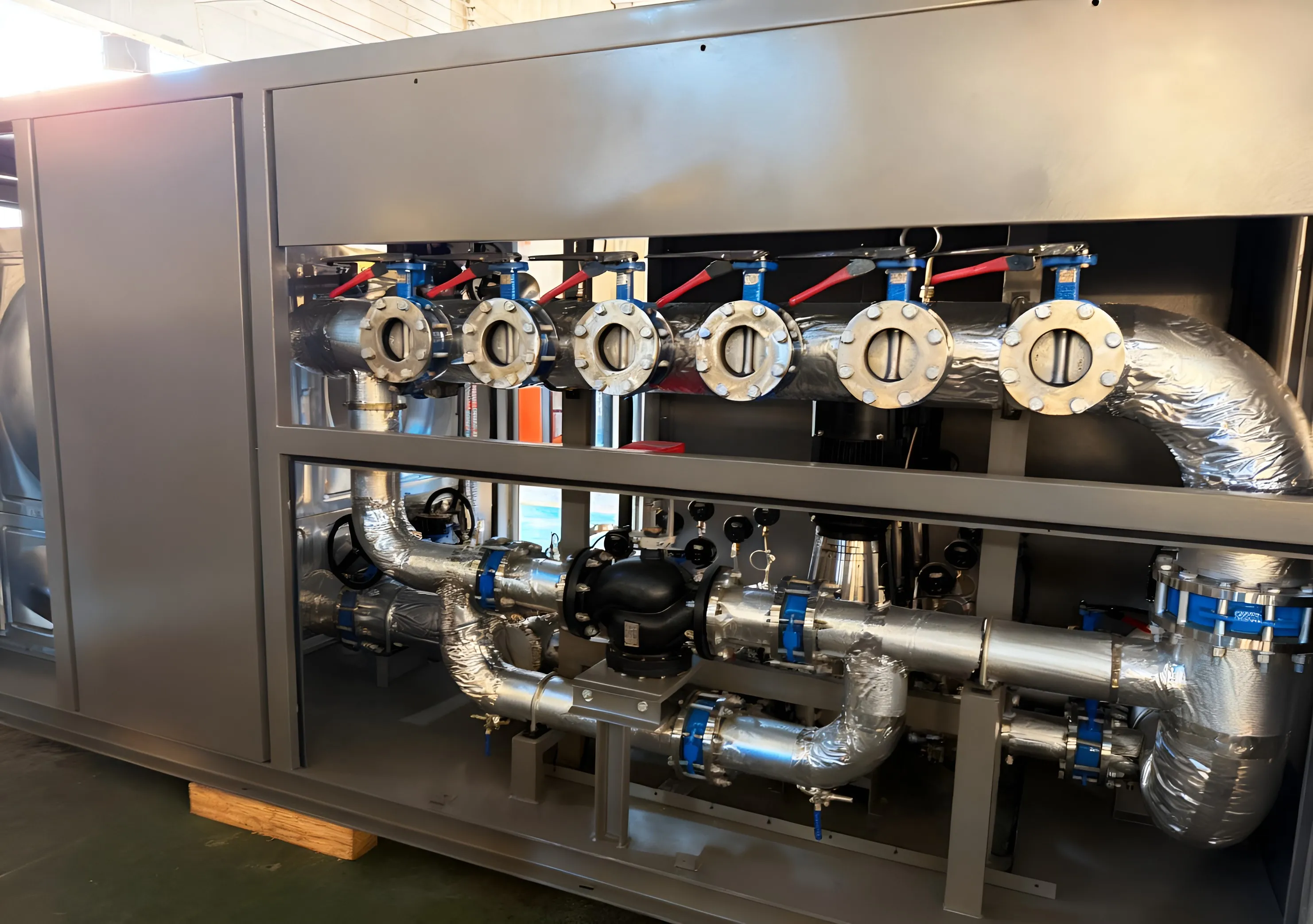 Flanged headers and insulated stainless pipework inside a pump-station enclosure.